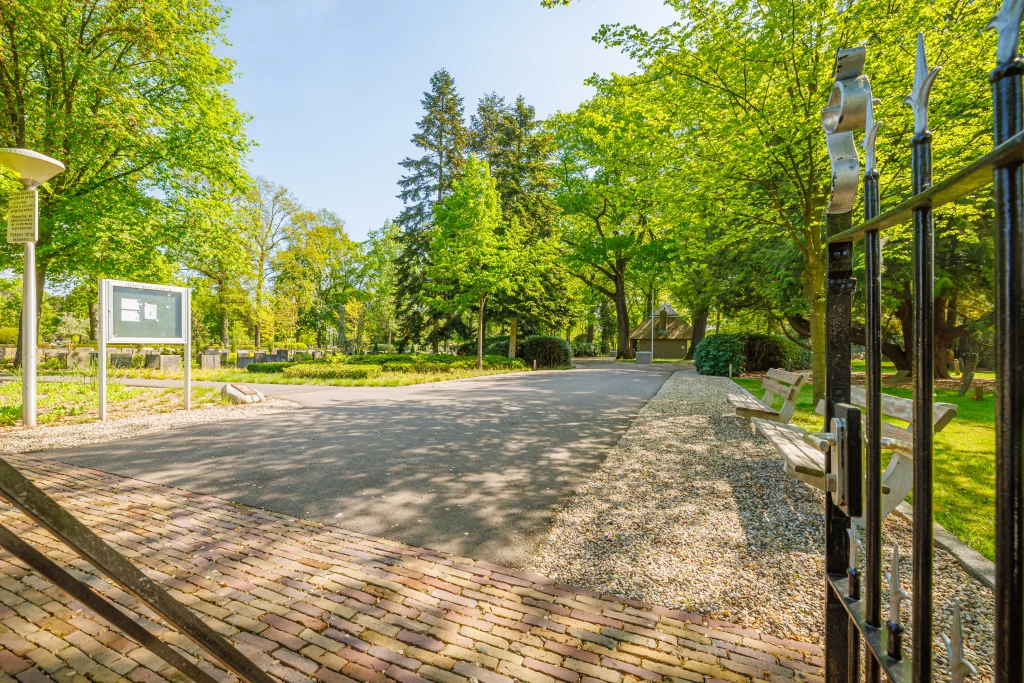 Ingang van de begraafplaats aan de Ninaberlaan met open poort, informatiebord en zitbank.